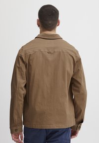 Veste en coton marron avec un col pointu, des poignets à bouton et une coupe droite. Présente un design de dos épuré sans poches visibles ni embellissements.