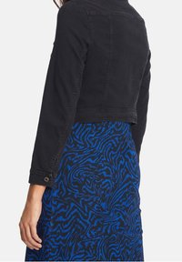 Svart denimjacka med croppad längd och långa ärmar, med en klassisk krage och knapprad, tillsammans med en blåmönstrad klänning.