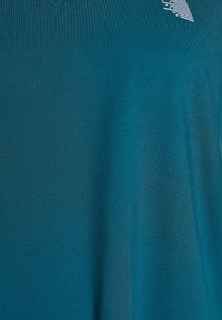 Teal short-sleeve shirt with a v-neck. Made from smooth fabric, it features a subtle white logo in the upper right corner.