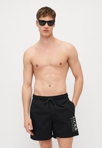 Fekete úszónadrág, elasztikus derékrésszel és zsinórral, oldalt fehér és zöld "JACK & JONES" logóval.