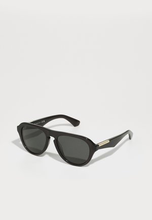 Óculos de sol de plástico preto com lentes escuras, formato retangular e um acabamento dourado nas hastes. Textura suave e design elegante.