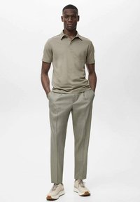 Jasnooliwkowa koszulka polo z kołnierzykiem, zestawiona z jasnoszarymi, dopasowanymi spodniami i neutralnymi sneakersami. Gładki materiał, slim fit.