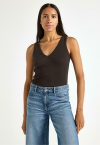 Brun, ribbet ærmeløs top med V-halsdesign, parret med højtaljede lyseblå vide jeans. Neutral baggrund.