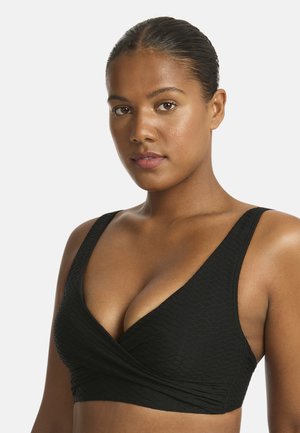 Kobieta o ciemnych włosach ułożonych w gładki kok, ubrana w fakturowany czarny wiązany top od bikini na jednolitym jasnym tle.