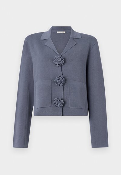 Chaqueta corta y texturizada en tela azul-gris con cuello de muesca, que presenta tres botones decorativos en forma de roseta y dos bolsillos frontales.