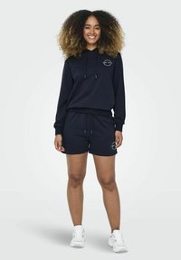 Felpa blu navy con cordini e logo, abbinata a pantaloni corti coordinati. Il materiale è morbido, presenta polsini a costine ed è comodo per l'abbigliamento casual.