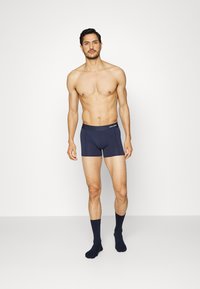 Boxer briefs in cotone blu navy con un morbido elastico in vita e una tasca frontale, indossati con calze coordinate fino al ginocchio, esposti su uno sfondo neutro.