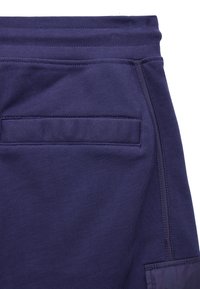 Gros plan sur le tissu d'un pantalon bleu marine montrant une poche arrière avec une fente horizontale et des coutures renforcées.