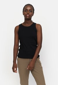 Top negru, cu nervuri, cu decolteu rotund și design fără mâneci, asortat cu pantaloni bej, tăiați, dintr-un material neted.