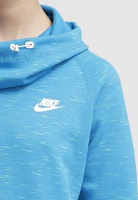 Blåprickig Nike-tröja med hög krage som har vita justerbara snörstopp, som visar övre delen av bröstet och axelområdet.