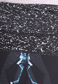 Leggings neri con una fascia grigia maculata, caratterizzati da motivi geometrici blu a contrasto e una finitura testurizzata. Dettagli di cucitura visibili.
