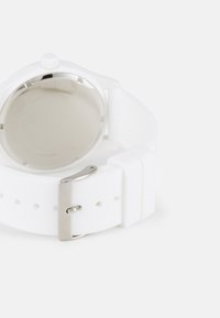 Montre en silicone blanche avec une boucle en métal argenté, présentant un boîtier circulaire lisse et un design minimaliste. Le dos affiche une surface brillante.