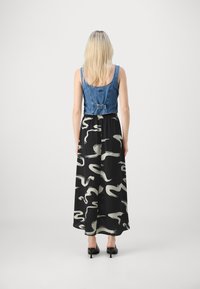Crop top en denim avec de larges bretelles et un buste ajusté sur une longue jupe noire ornée de motifs abstraits blancs, associé à des talons noirs.