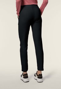 Pantaloni neri aderenti con una texture liscia e design alla caviglia, abbinati a sneakers sportive bianche e una maglietta rosa.