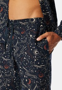 Conjunto de pijama en azul marino con patrones celestiales en crema y óxido, cuenta con una cintura elástica, cordón y bolsillos laterales.