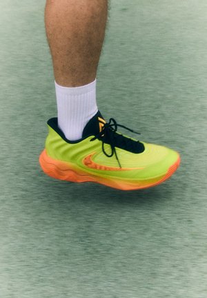 Limonkowo-zielony i pomarańczowy but sportowy z teksturowanym wzorem, czarnymi sznurowadłami i logo, w połączeniu z białą skarpetką za kostkę.