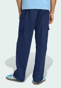 Navy blue cargo pants with side pockets, featuring a loose fit and a textured fabric. Worn with light blue footwear and a casual top.