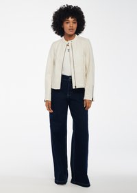 Giubbotto bomber in pelle crema con polsini con cerniera, abbinato a pantaloni in denim scuri a gamba larga. L'outfit presenta una maglietta bianca aderente sotto.