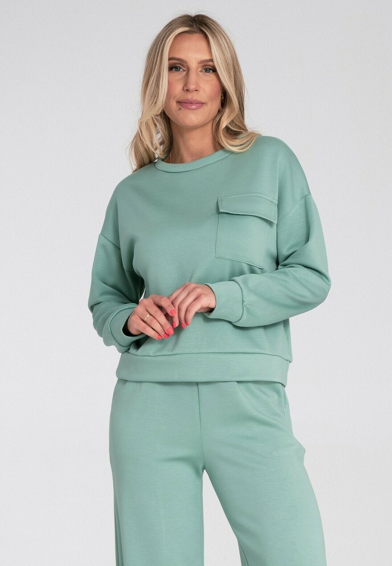 Miętowa, długorękawowa bluza z okrągłym dekoltem, kieszenią z przodu i ściągaczami, w połączeniu z pasującymi spodniami. Miękka tekstura materiału.