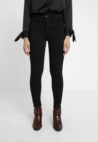 Black high-waisted skinny jeans with a smooth texture and slim fit, paired with brown crocodile-embossed ankle boots.