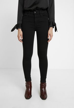 Pantalones vaqueros ajustados de tiro alto en negro con una textura suave y un corte delgado, combinados con botas de tobillo en marrón con estampado de cocodrilo.