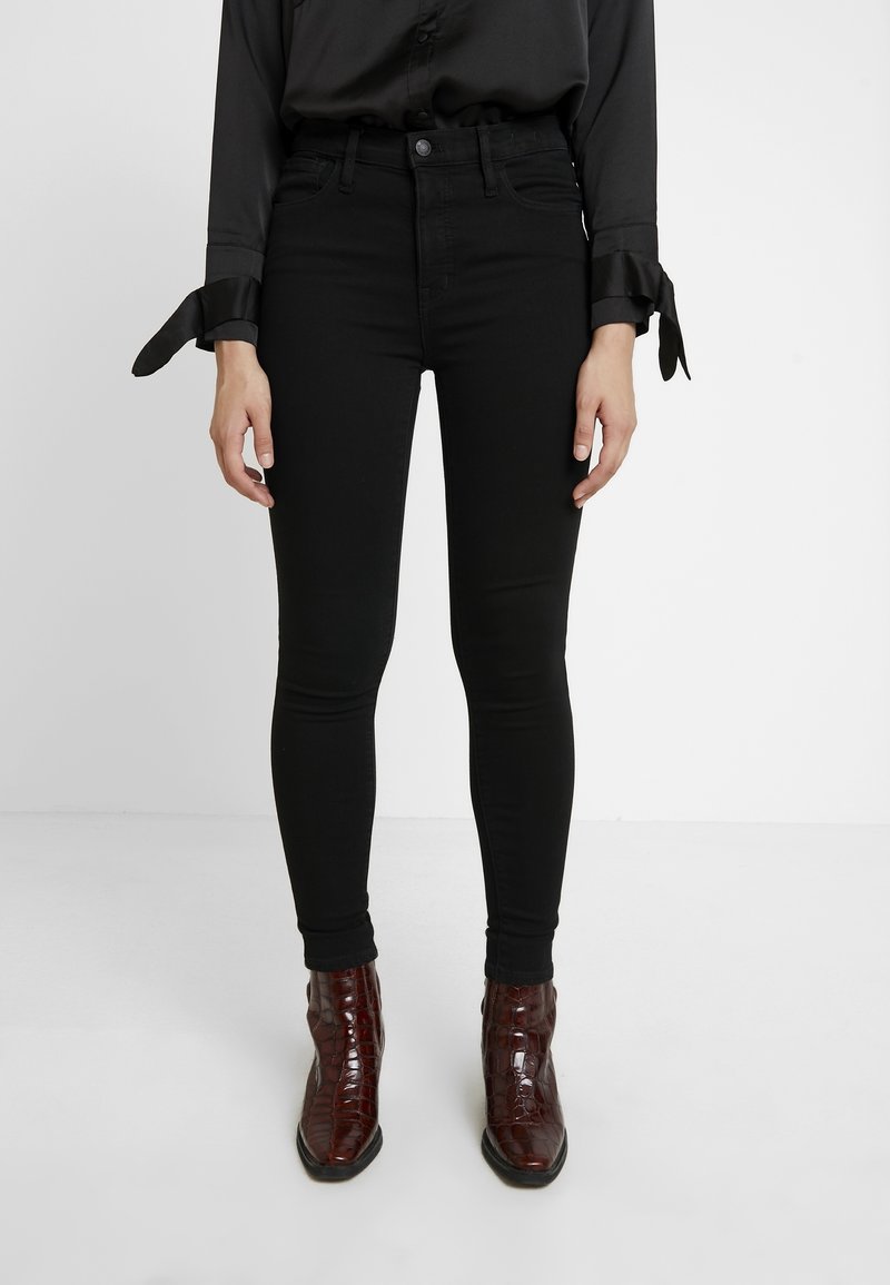 Black high-waisted skinny jeans with a smooth texture and slim fit, paired with brown crocodile-embossed ankle boots.