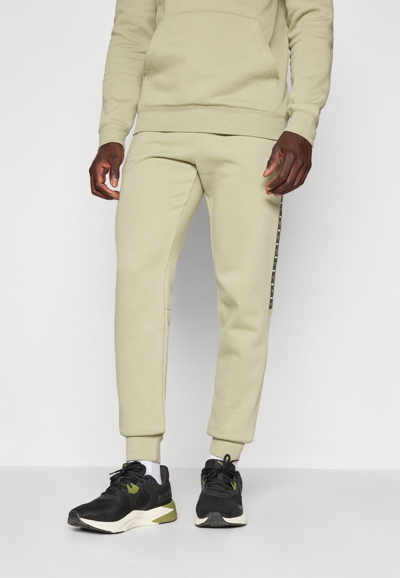 Lichtgroene katoenen hoodie met een voorzak, gecombineerd met bijpassende joggers met een zijstreep. Zwarte en olijfgroene sneakers maken de look compleet.