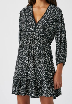 Schwarzes Blumenkleid mit weißen Mustern, V-Ausschnitt, 3/4-Ärmel, gerafftem Oberteil und rüschendem Saum. Hergestellt aus leichtem Stoff.