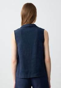 Mouwloos marineblauw linnen top met een kraag, textuurstof en rechte snit, met een achterkant die de bovenlichaamdetails toont.