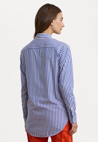 Blauw-wit gestreepte longsleeve shirt met een puntige kraag, gebogen zoom en knoopmanchetten, gecombineerd met oranje broek.