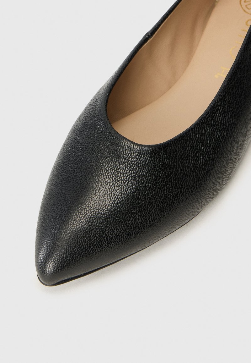 Zapato plano de cuero negro con un acabado texturizado, punta afilada y un interior suave. El diseño presenta un empeine bajo y un detallado minimalista.