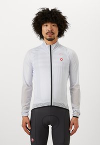 Veste de cyclisme légère blanche avec manches longues et fermeture éclair sur le devant. Présente un logo rouge sur la poitrine et des détails texturés. Cuissards de cyclisme noirs.