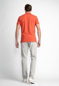 Oranje kortemouw polo-shirt, effen kleur, gecombineerd met lichtgrijze broek. De outfit heeft een casual pasvorm en een minimalistisch ontwerp.