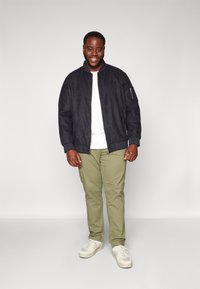 Chaqueta bomber de color marino en material suave parecido al ante, combinada con pantalones verde claro y zapatillas crema. La chaqueta cuenta con un bolsillo con cremallera y puños acanalados.