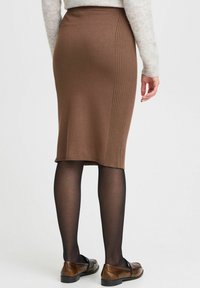 Jupe crayon tricotée marron avec des détails côtelés sur le côté, associée à des collants noirs et des mocassins marron. Texture lisse, longueur sous le genou.