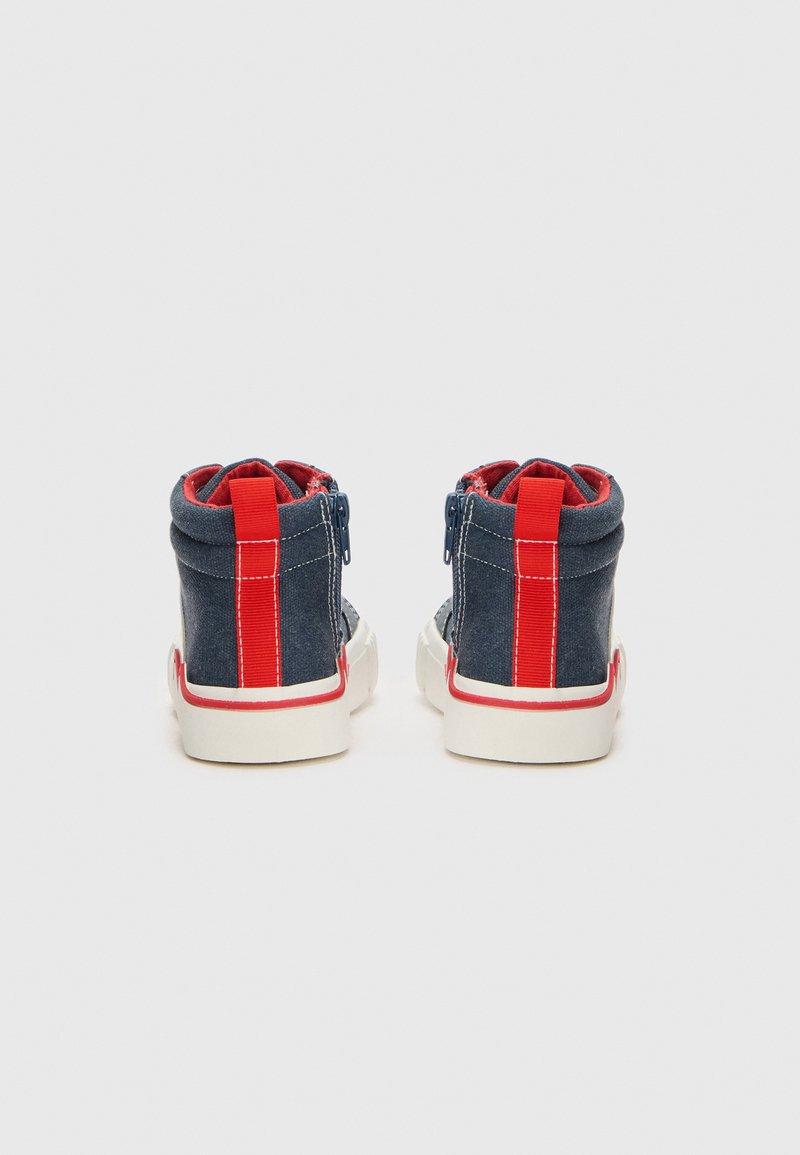 Baskets montantes en denim navy avec des accents rouges et une semelle blanche. Dotées d'une fermeture éclair et d'un renfort au niveau du talon et de la cheville.