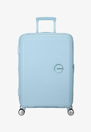 Valigia rigida blu chiaro con texture a cerchi concentrici, due ruote e manico retrattile. Presenta un dettaglio del logo argentato.