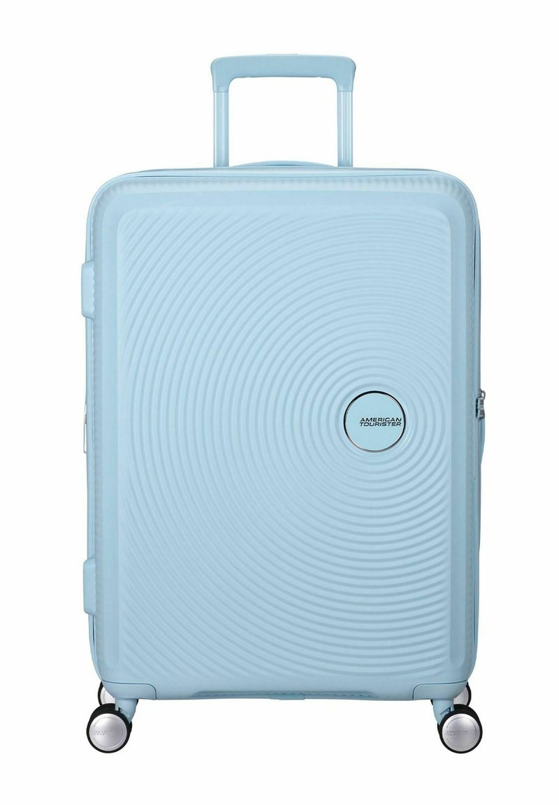 Valigia rigida blu chiaro con texture a cerchi concentrici, due ruote e manico retrattile. Presenta un dettaglio del logo argentato.