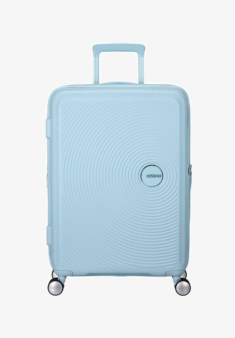 Valigia rigida blu chiaro con texture a cerchi concentrici, due ruote e manico retrattile. Presenta un dettaglio del logo argentato.