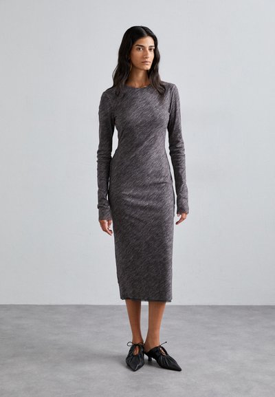 Robe à manches longues, grise chinée, avec une silhouette ajustée, faite d'un tissu doux et extensible. Des chaussures noires avec des lacets à l'avant viennent parfaire le look.