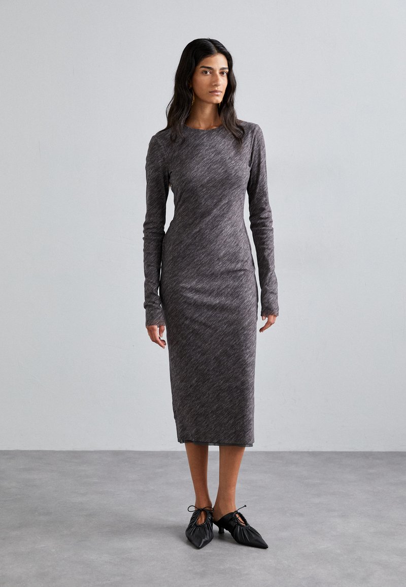 Long-sleeve, heather gray dress with a fitted silhouette, made of soft, stretchy fabric. Black shoes with ties at the front complete the look.