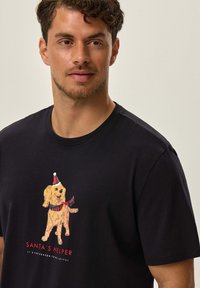 Czarna koszulka z krótkim rękawem z rysunkowym psem w czapce Mikołaja, z napisem "POMOCNIK MIKOŁAJA" poniżej w czerwono-białym kolorze.