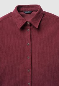 Camicia in corduroy bordeaux con colletto button-down, caratterizzata da strisce verticali texture e bottoni grigi lungo la parte anteriore. Etichetta della marca: Calliope.