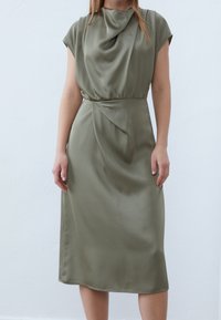 Satijnen midi-jurk in olijfgroen met mouwloze cap sleeves, gedrapeerde col met watervalhals, gerimpelde taille en geplooide accenten. Soepele textuur, nauwsluitende pasvorm.