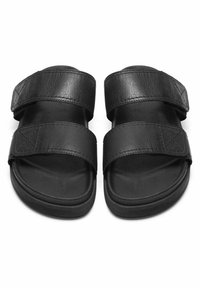 Sandales à slide noires avec deux brides en cuir texturé et une semelle en caoutchouc plate, au design simple sans aucun élément métallique visible.