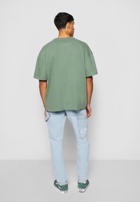 Grønn oversized bomullst-skjorte med rund hals, sammen med lyseblå jeans med logodetalj. Uformell fottøy kompletterer stilen.