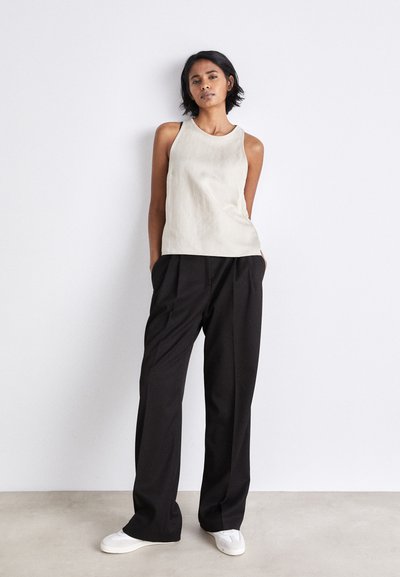 Light beige sleeveless top with a round neckline paired with black wide-leg trousers and white sneakers on a neutral background.