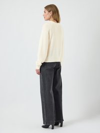 Maglione di lana beige chiaro con maniche lunghe, abbinato a pantaloni in denim neri a vita alta e a gamba larga, visto da dietro.