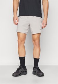Light grey shorts with a smooth texture and elastic waistband, paired with black athletic shoes and crew socks. Subtle logo detail on the shorts.