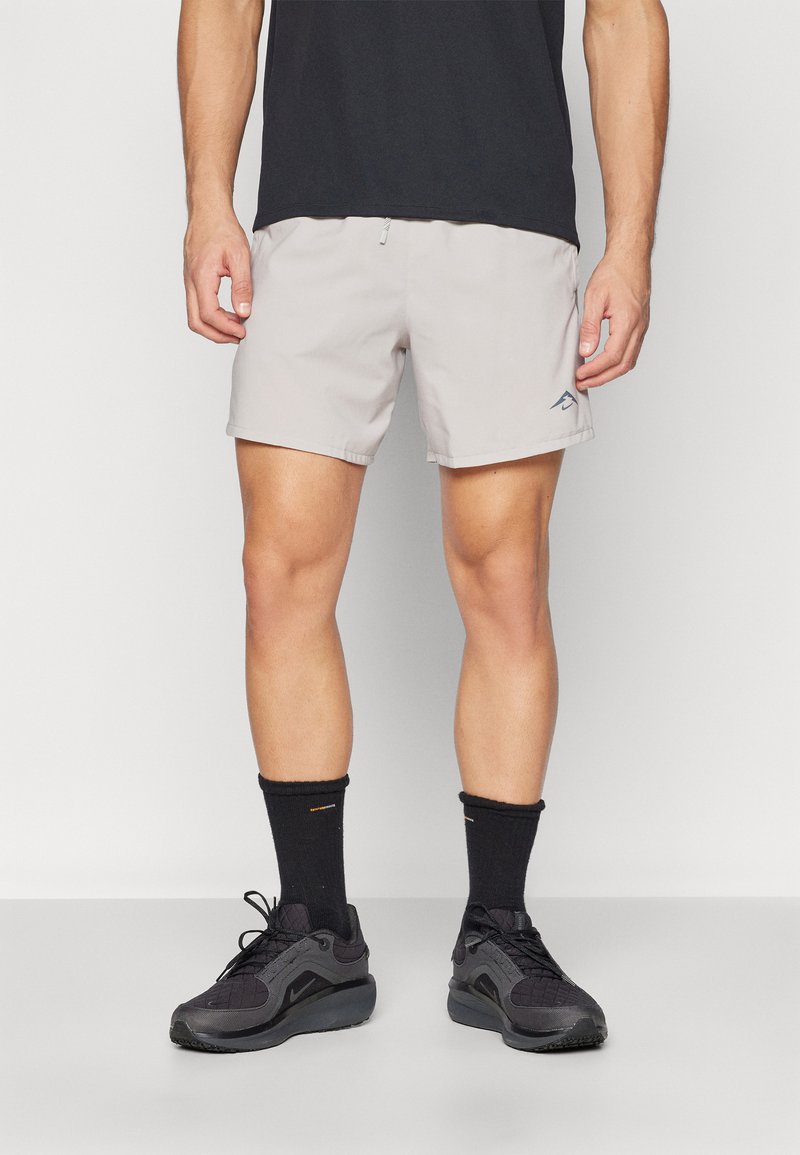 Light grey shorts with a smooth texture and elastic waistband, paired with black athletic shoes and crew socks. Subtle logo detail on the shorts.